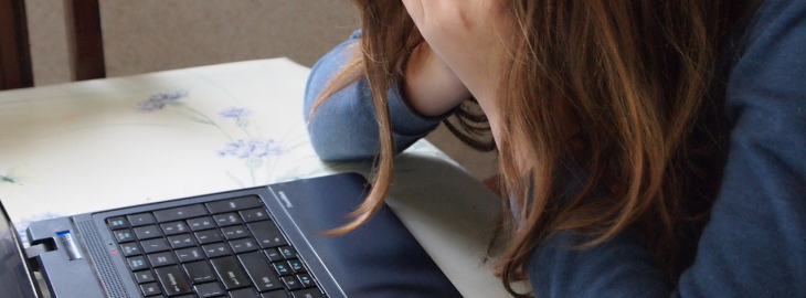dziewczyna pochylona nad komputerem, trzymająca twarz w dłoniach